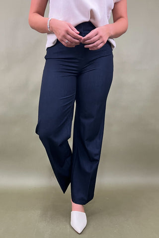 Person wearing navy pants and a white top on a beige background