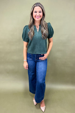 Woman wearing a green top and blue jeans against a plain background