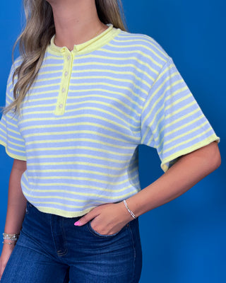 A woman wearing a short-sleeve henley top with light blue and pale yellow horizontal stripes, paired with dark blue jeans