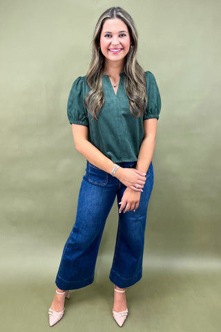Woman wearing a green blouse and blue jeans against a green background