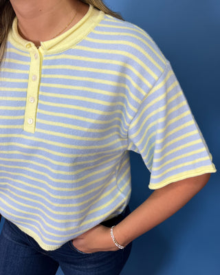 A close-up of a person wearing a short-sleeve ribbed henley top with light yellow and light blue horizontal stripes