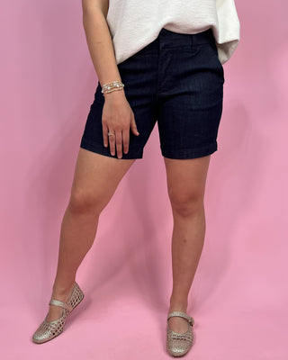 Person wearing navy shorts and silver shoes on a pink background
