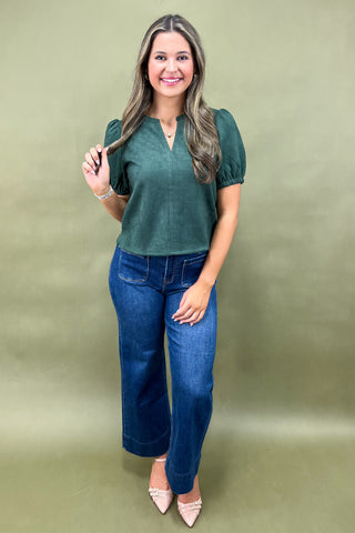 Woman wearing a green top and blue jeans against a green background