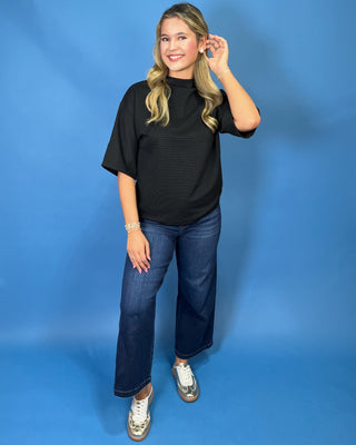 A woman modeling a black short-sleeve mock neck t-shirt, dark blue wide-leg jeans