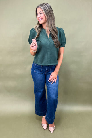 Woman wearing a green top and blue jeans against a plain background