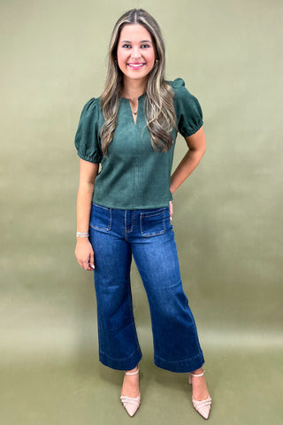 Woman wearing a green top and blue jeans against a green background