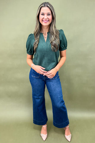 Woman wearing a green top and blue jeans against a green background