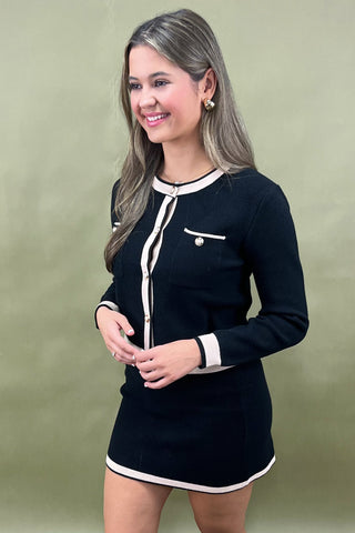 Woman wearing a black dress with white trim against a green background