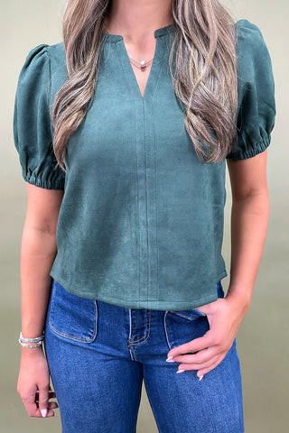 Woman wearing a teal blouse with puff sleeves and blue jeans against a neutral background