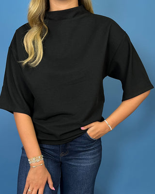 A woman wearing a black short-sleeve ribbed mock neck top and blue jeans