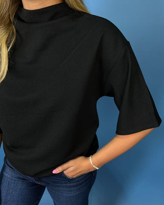 A person wearing a black ribbed mock neck top with elbow-length sleeves, paired with blue jeans