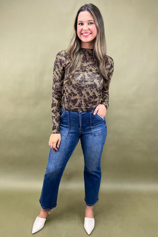Woman wearing a camouflage long-sleeve top and blue jeans against a green background
