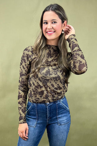 Woman wearing a patterned long-sleeve top and blue jeans against a green background