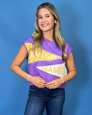 A smiling woman with blonde hair wearing a purple knit sweater with yellow and white graphic text that reads 'GAMEDAY' and blue jeans.