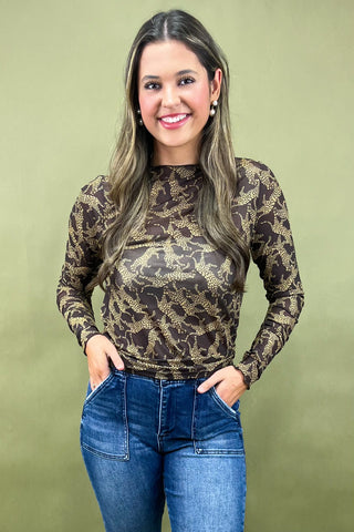 Woman wearing a leopard print long-sleeve top and blue jeans against a green background