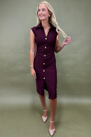 Woman wearing a purple dress with buttons against a plain background