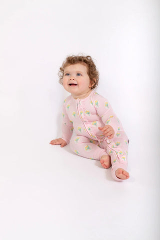 A baby wearing a light pink footless sleeper with a green and yellow leaf pattern, sitting against a plain white background.
