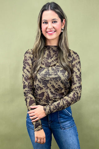 Woman wearing a patterned long-sleeve top and jeans against a green background