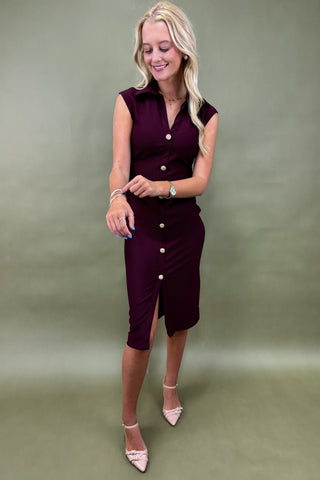 Woman wearing a sleeveless burgundy dress with buttons against a green background