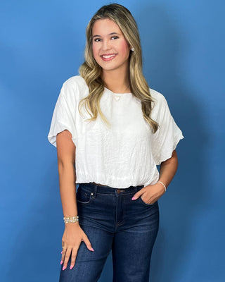 A woman with blonde hair wearing a white short-sleeve textured blouse and dark blue jeans