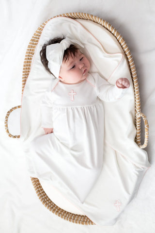 Baby wrapped in a white blanket with a hood, lying in a wicker basket on a light gray background.