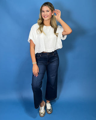 A woman modeling a white short-sleeve blouse and dark blue wide-leg jeans