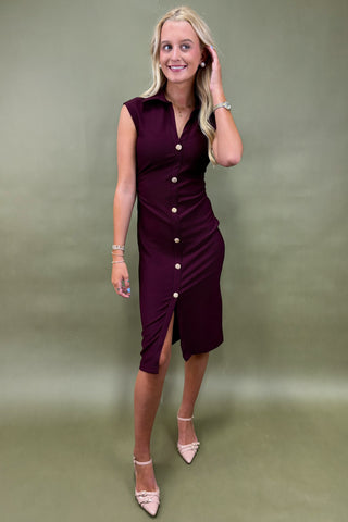 Woman wearing a burgundy dress with buttons against a plain background
