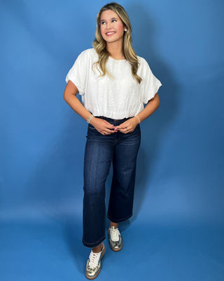 A woman modeling a white short-sleeve blouse and dark blue wide-leg jeans with metallic sneakers