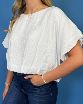 A woman wearing a white short-sleeve top with a crinkled texture and dark blue jeans