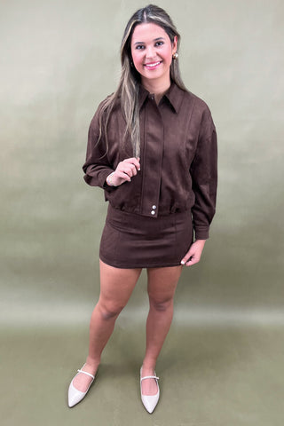 Woman wearing a brown outfit with a matching jacket and skirt on a green background