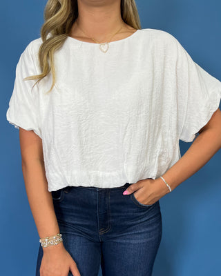 A woman wearing a white short-sleeve crinkled blouse and dark blue jeans