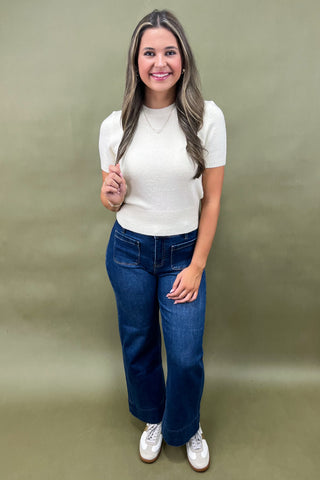 Woman wearing a white t-shirt and blue jeans against a green background