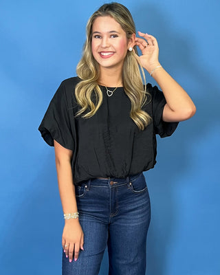 A woman modeling a black short-sleeve top and dark blue wide-leg jeans