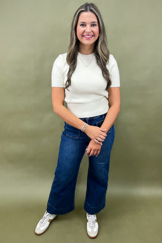 Woman wearing a white top and blue jeans against a green background