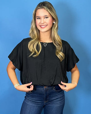 A woman modeling a black short-sleeve blouse with ruffled sleeves and dark blue wide-leg jeans
