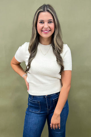 Woman wearing a white top and blue jeans against a green background