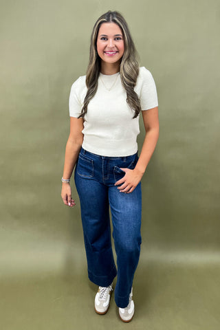 Woman wearing a white top and blue jeans against a green background