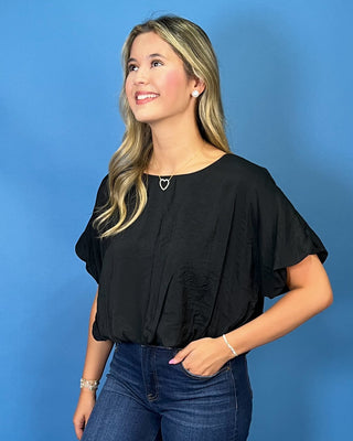 A woman modeling a black short-sleeve blouse with ruffled sleeves and dark blue wide-leg jeans