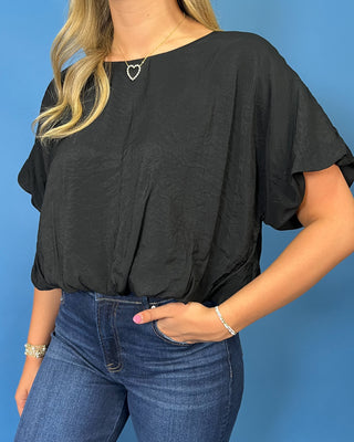 A woman modeling a black short-sleeve blouse with ruffled sleeves and dark blue wide-leg jeans