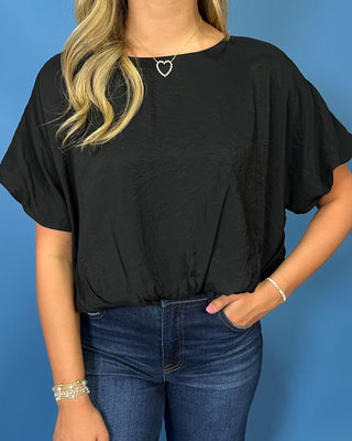 A woman modeling a black short-sleeve blouse with ruffled sleeves and dark blue wide-leg jeans