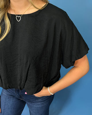 A woman wearing a loose black short-sleeve top with a textured crinkled fabric, paired with blue jean