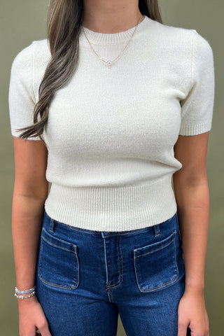 Person wearing a white short-sleeve sweater and blue jeans against a green background