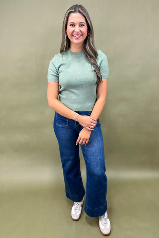 Woman wearing a green sweater and blue jeans against a beige background