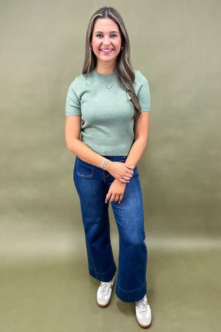 Woman wearing a green top and blue jeans against a beige background