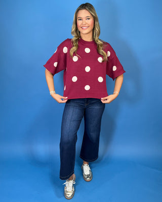 Burgundy short sleeve knit sweater top with oversized ivory polka dots, a round neckline, and ribbed trim.