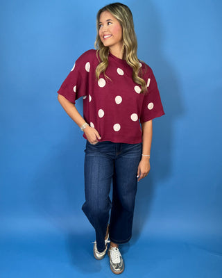 Burgundy short sleeve knit sweater top with oversized ivory polka dots, a round neckline, and ribbed trim.