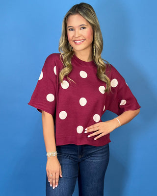 Burgundy short sleeve knit sweater top with oversized ivory polka dots, a round neckline, and ribbed trim.