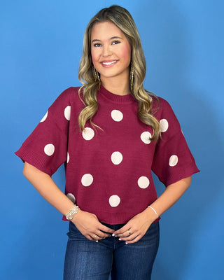Burgundy short sleeve knit sweater top with oversized ivory polka dots, a round neckline, and ribbed trim.