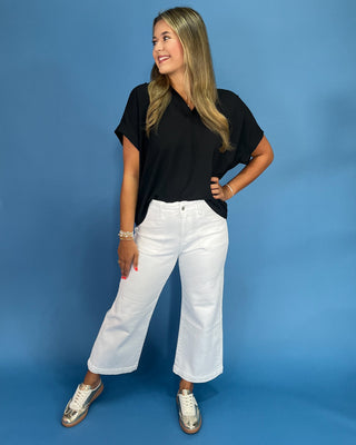 Woman wearing a black t-shirt and white pants against a blue background