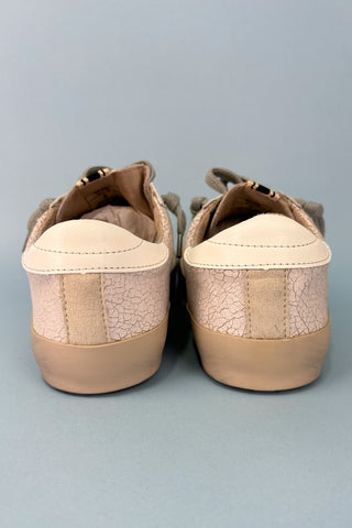 Pair of beige sneakers with cracked sole on a gray background